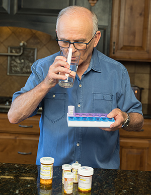 Hombre tomando pastillas en la cocina.